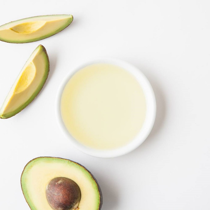 A bowl of avocado oil with some slices
                of avocado on a white background