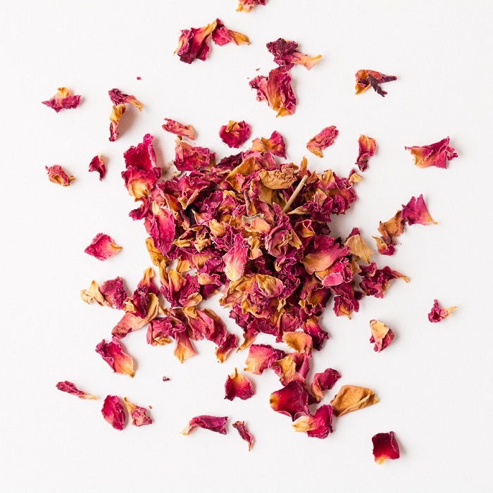 Dried red rose petals on a white
                background