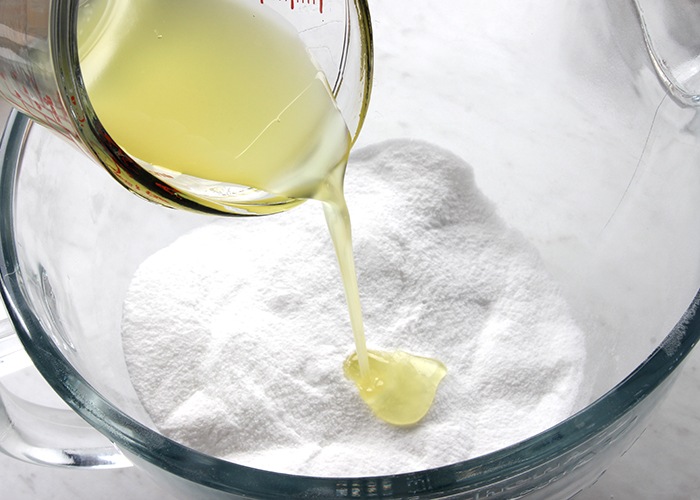 a gloved
                hand pouring oil into a powdered bath bomb mixture