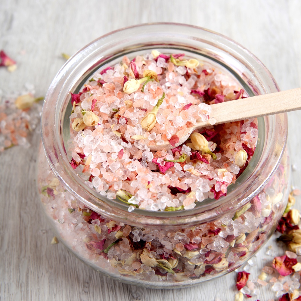 A jar of pink bath salts with rose petals